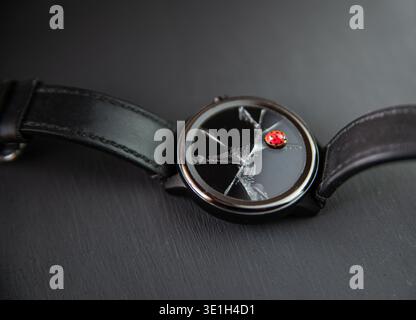 The minimalist photo shows a wristwatch with a black strap and broken glass, on the dial of which a red ladybug sits like a symbolism, contrasting wit Stock Photo