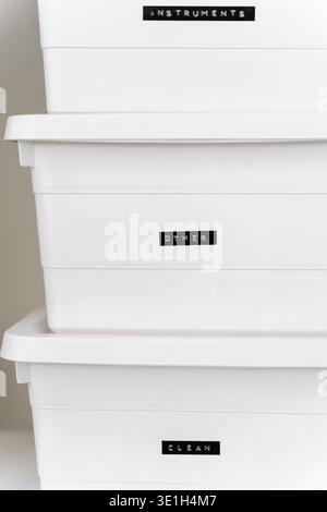 Minimal white storage boxes stacked on shelf with labels for organization. Clean home storage concept with plastic containers for office supplies, cle Stock Photo