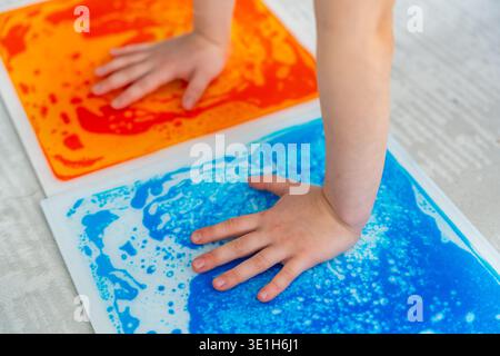 Child hands pressing colorful sensory gel mats creating moving patterns during tactile play. Sensory stimulation and occupational therapy concept for Stock Photo