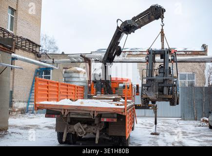 Loading a forklift onto a truck, crane, carrier, manipulator with a boom. Forklift hanging in the air on the boom of a crane. High quality photo Stock Photo