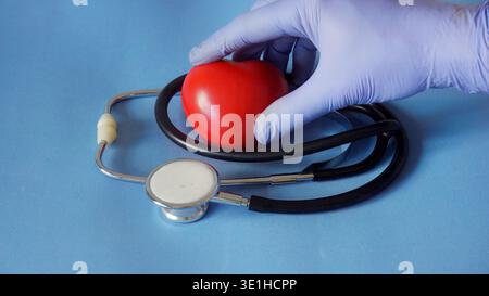 Doctor hand in blue glove holding a red heart near a stethoscope on blue background Stock Photo