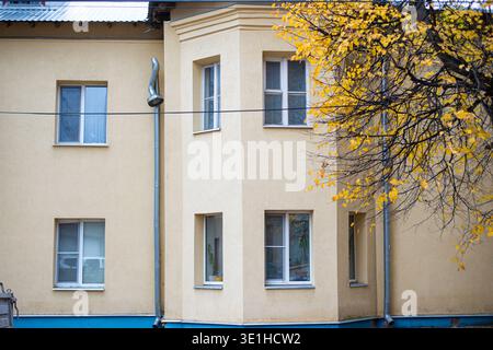 The facade of the building is plastered and painted in beige pastel color. Autumn tree with yellow leaves in the foreground. High quality photo Stock Photo