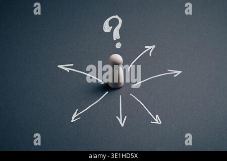 Wooden pawn figurine surrounded by hand-drawn white arrows and a question mark on a dark background, symbolizing decision making, choices and uncertai Stock Photo