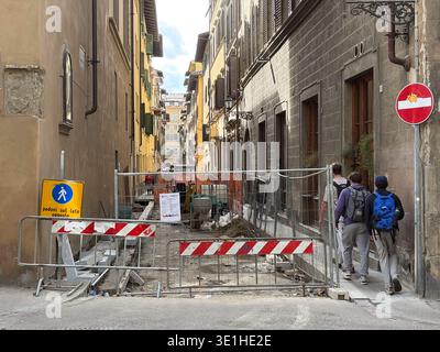 Roadworks block a narrow street in Florence, Italy. Three backpackers detour past barriers and signage in historic city center. Stock Photo