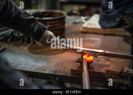 In the blacksmith's workshop, the blacksmith is leveling the red-hot metal with a hammer. A red-hot piece of metal with scale is being prepared for hardening. High quality photo Stock Photo