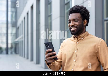 Smiling man enjoying a moment outdoors while looking at his smartphone, connecting with people, and managing his schedule in a modern urban environment Stock Photo