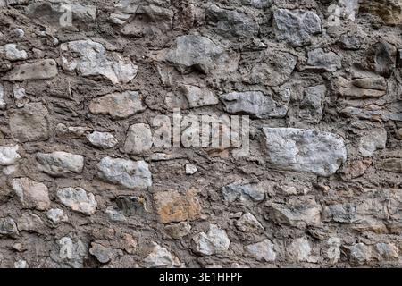 Old irregular stone wall with rough natural stones and weathered rural masonry creating a rustic textured background in Canale di Tenno Trentino Alto Stock Photo