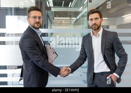 Two confident businessmen in formal wear are shaking hands, symbolizing agreement, partnership, and successful collaboration during a business meeting Stock Photo