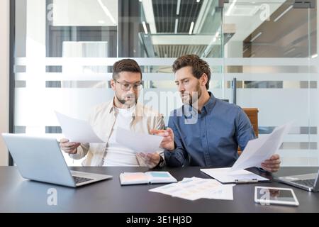 Two business colleagues working together, discussing documents and analyzing data during a corporate meeting in a contemporary office setting, demonst Stock Photo