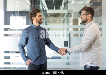 Two businessmen smiling and shaking hands in a modern office, sealing a partnership agreement that symbolizes trust, cooperation, professional success Stock Photo