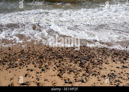 Gentle waves breaking on a pebble and sand shoreline leaving light foam streakes Stock Photo