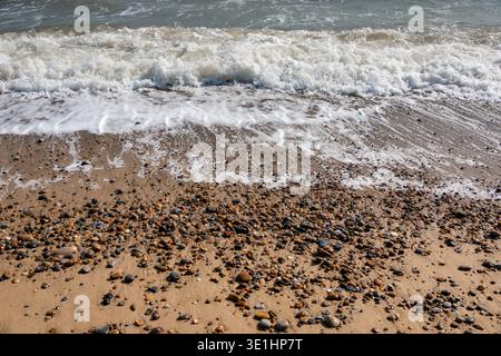 Gentle waves breaking on a pebble and sand shoreline leaving light foam streakes Stock Photo