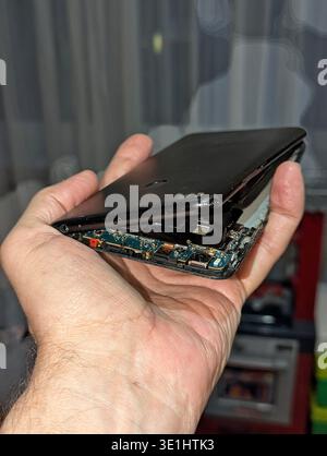 DIY Repair Attempt With Bent Smartphone Held In Hand, Exposed Cables And Missing Screws Visible, No Protective Gear, Livingroom Backdrop Hints At Amat Stock Photo