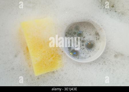 mug and sponge in soap suds in washing up bowl Stock Photo