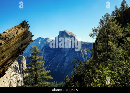 Half Dome granite peak rising above forest and cliffs in Yosemite National Park under clear blue sky, California USA Stock Photo