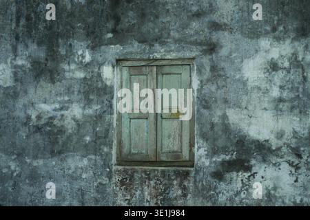 Old closed wooden window on a weathered concrete wall with textured surface in an outdoor environment Stock Photo