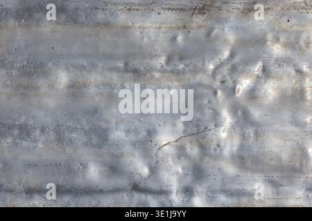 Rough aluminum sheet displays textured surface with scratches and damage. Outdoor industrial setting highlights weathered appearance under bright daylight. Stock Photo