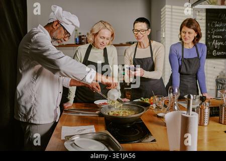 Middle Aged Man Teaching Women Cooking during Class Stock Photo