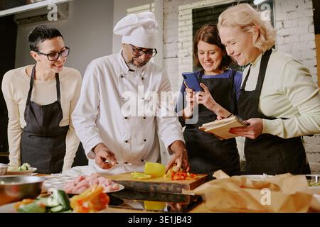 Middle Aged Man Teaching Cooking Class to Diverse Women Stock Photo