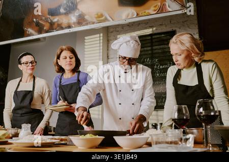 Middle Aged Man Teaching Cooking Class to Diverse Middle Aged Women Stock Photo