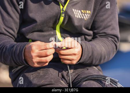 Close-up of hands working on a wire, in black workwear with lime green zipper, PV assembly at OBI Baumarkt, Muehlacker, Enzkreis, Germany Stock Photo