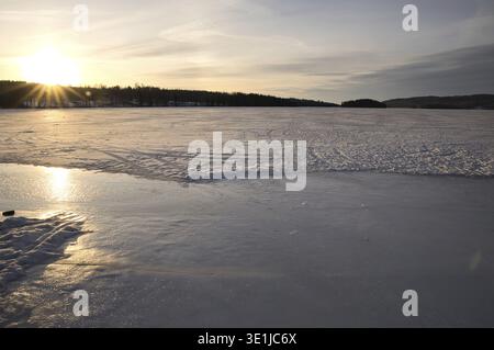 Sunlight reflecting on the frozen surface of Lake Aer in Dalsland, Sweden, golden sunset over a vast ice landscape with snow-covered shores and a wond Stock Photo