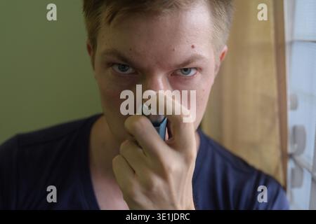 Portrait of young handsome man using asthma inhaler at home Stock Photo