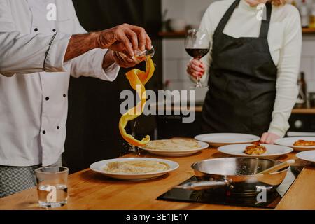 Middle Aged Caucasian Woman Observing Chef Garnishing Dish during Cooking Class Stock Photo