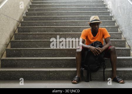 Young black African tourist man thinking while sitting on the staircase leading towards the underground train station of Bangkok Thailand Stock Photo
