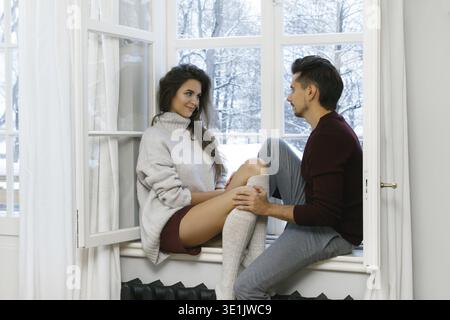 Young lovely couple sitting on the window sill at cold snowy day Stock Photo