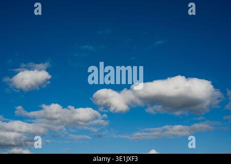 Fluffy white clouds float in a clear blue sky, with wispy clouds adding texture to the scene, creating a peaceful and open outdoor environment Stock Photo