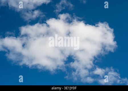 Fluffy white clouds float in a clear blue sky, showcasing a bright and sunny day with no visible obstructions or weather disturbances Stock Photo