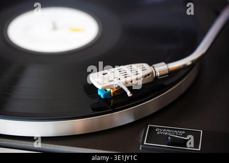 Close-up view of a turntable featuring a silver tonearm and stylus resting on a black vinyl record, highlighting the precision of the audio equipment Stock Photo