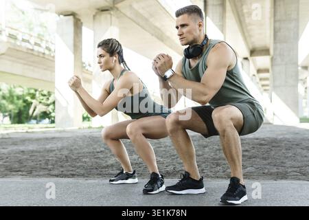 Athletic couple and fitness training outdoors. Man and woman doing squats during street workout Stock Photo