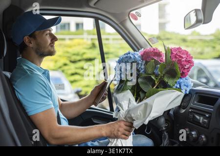 Courier inside the white van during flowers delivery is waiting for a client Stock Photo