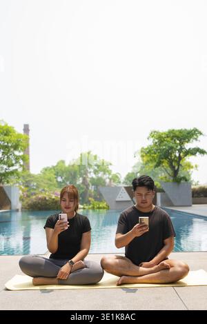 Young Asian couple doing yoga exercise next to swimming pool during summer Stock Photo