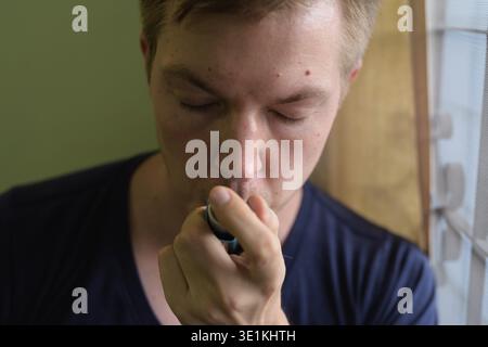 Portrait of young handsome man using asthma inhaler at home Stock Photo