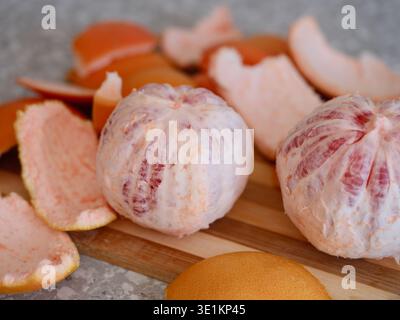 Two peeled whole grapefruits sit on a wooden cutting board surrounded by pieces of citrus peel. Stock Photo