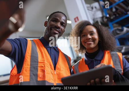Workers in an industrial plant, a senior employee holding a digital tablet, explaining to a new colleague how the machines work. Stock Photo