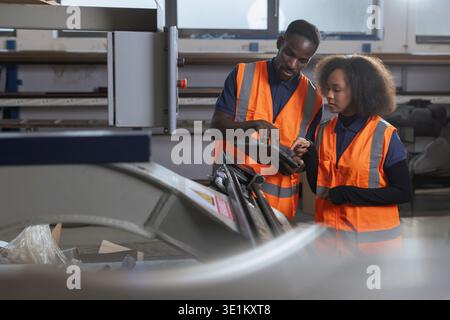 Two labour workers in industrial plant, looking at a tablet, discussing production and digital technology integration in factory operations. Stock Photo