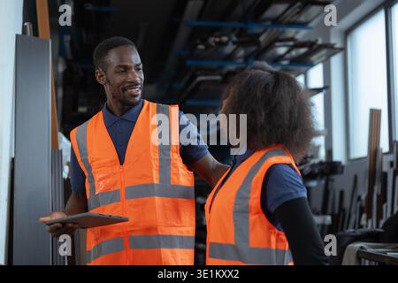 Two labour workers in industrial plant, looking at a tablet, discussing production and digital technology integration in factory operations. Stock Photo