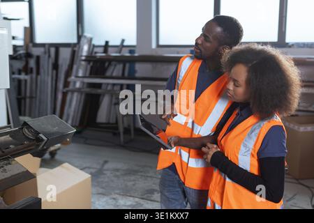 Workers in an industrial plant, a senior employee holding a digital tablet, explaining to a new colleague how the machines work. Stock Photo