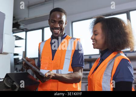 Workers in an industrial plant, a senior employee holding a digital tablet, explaining to a new colleague how the machines work. Stock Photo