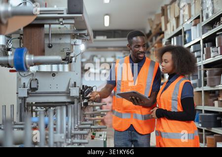 Technician african american workers wearing an orange safety vest using a tablet to control operating machinery at metal factory. Stock Photo