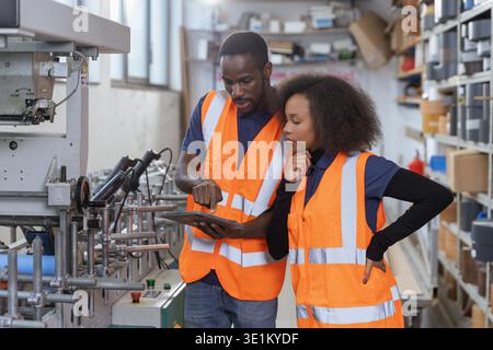 Two african american workers in the metal industry using a tablet for equipment diagnostics and digital checklists on the production line. Stock Photo