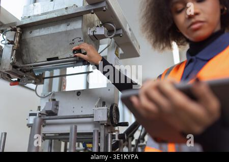 African American woman, worker in the metal industry using a tablet for equipment diagnostics and digital checklists on the production line. Stock Photo