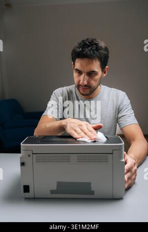 Vertical portrait of man performing printer maintenance, wiping dust off office laser printer, ensuring technology hygiene, cleaning and servicing Stock Photo