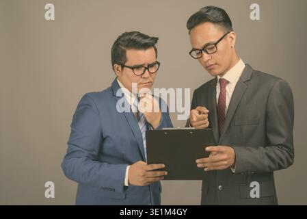 Studio shot of young multi-ethnic businessman and young Indian businessman together against gray background Stock Photo