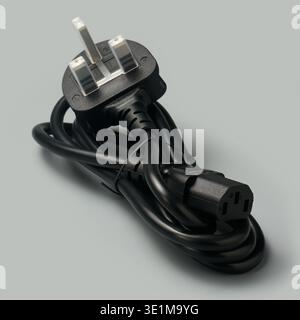 coiled black power cable with uk three-pin plug and iec connector isolated gray background, electronic lead for computer hardware Stock Photo