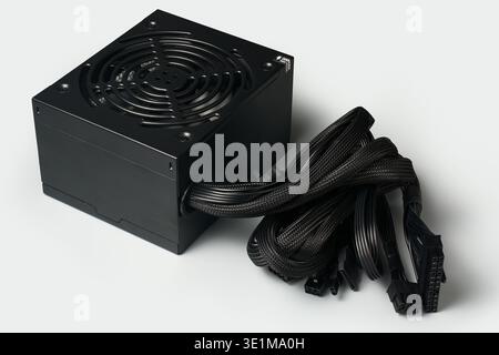 black atx pc power supply unit with cooling fan and bundled cables isolated light gray background, computer hardware electrical component, angle view Stock Photo